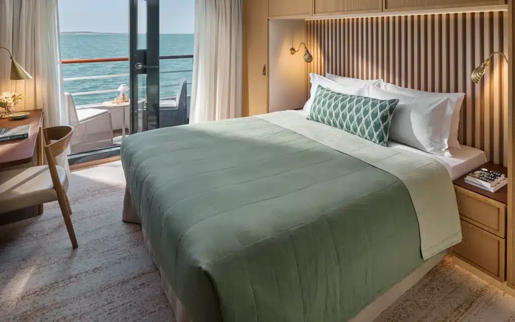 A stateroom aboard Paspaley Pearl with sage green bedding and ocean-view balcony
