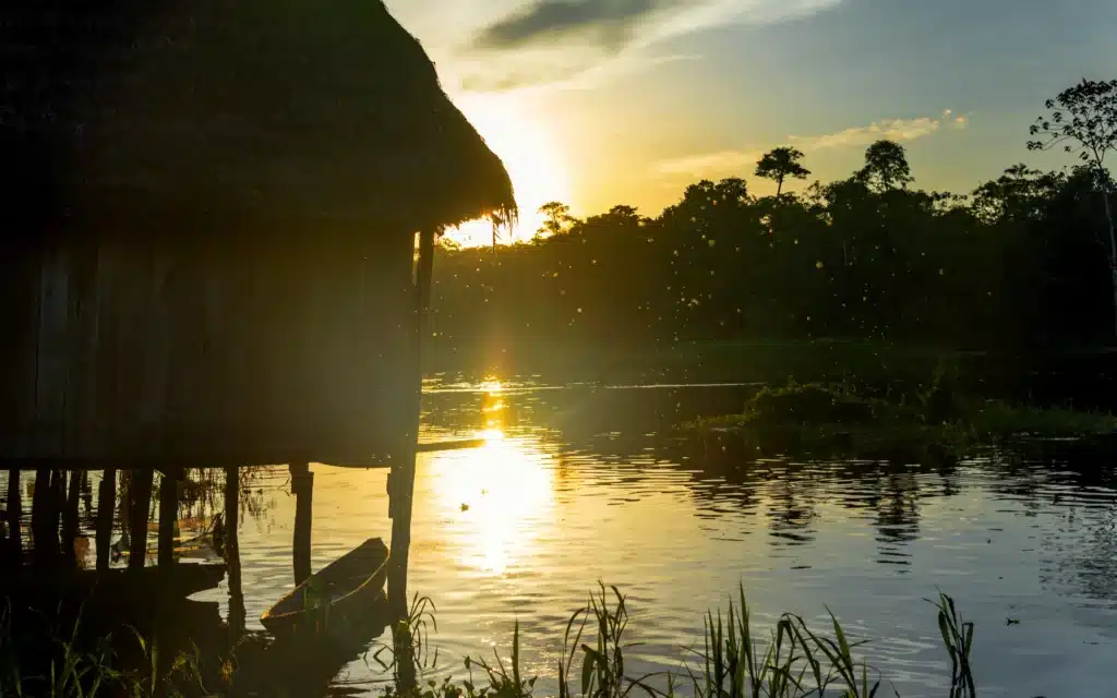 Silhouette of a thatched stilt house on the Amazon river at sunset