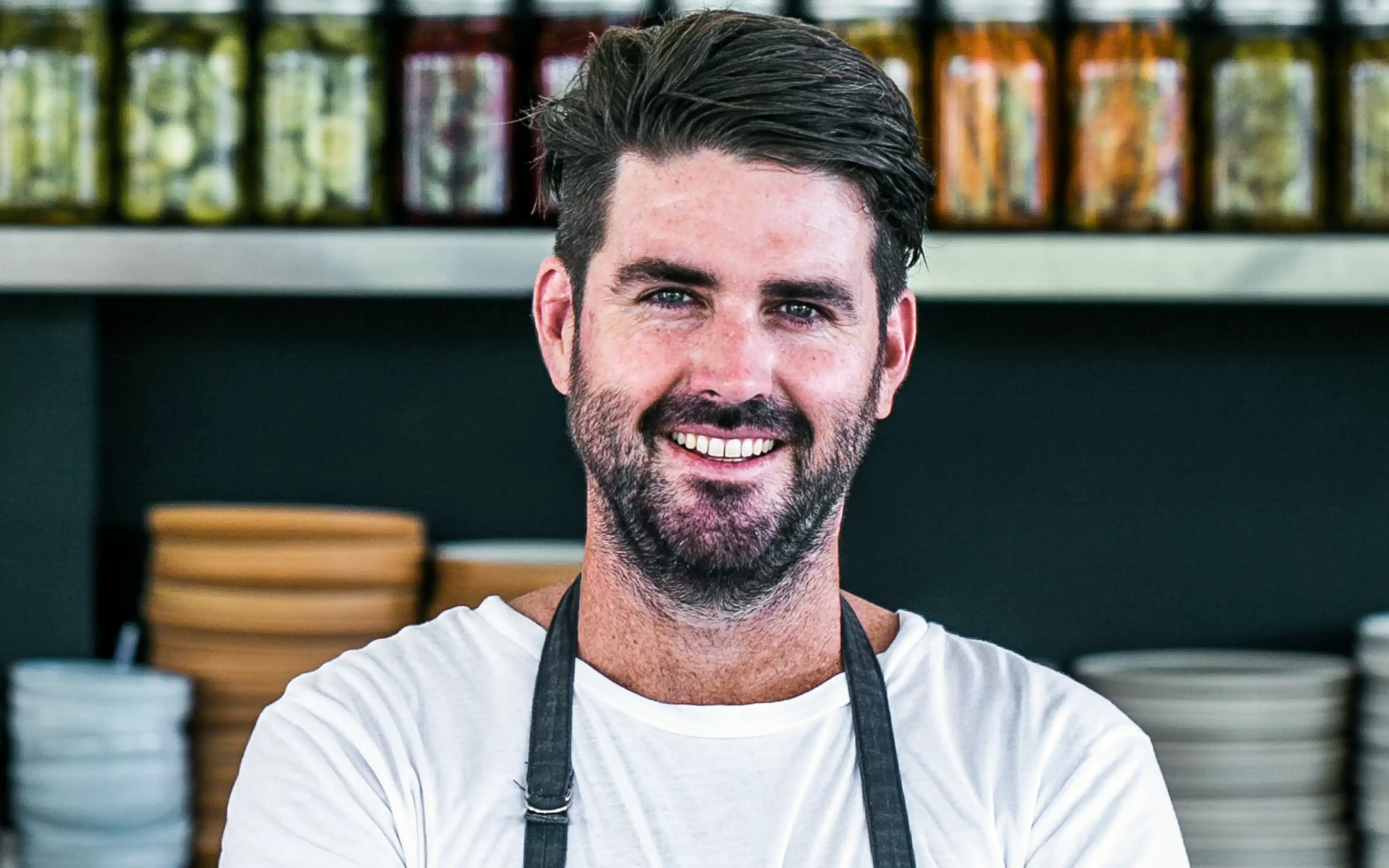 Chef Benjamin Cross smiling in kitchen with spice jars