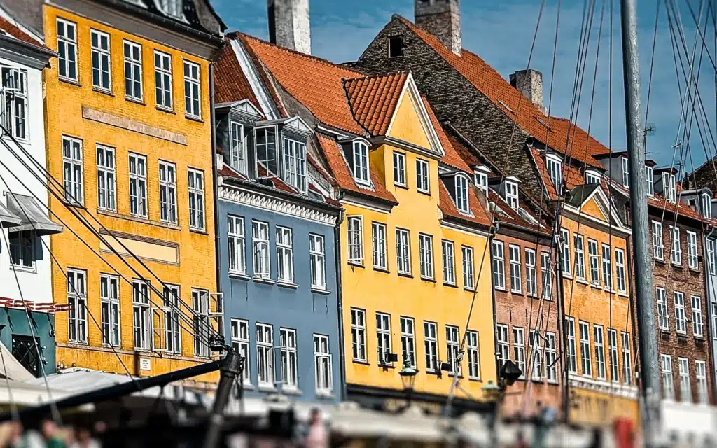 Colorful gabled townhouses with red-tiled roofs line Nyhavn harbor in Copenhagen behind the masts of moored ships