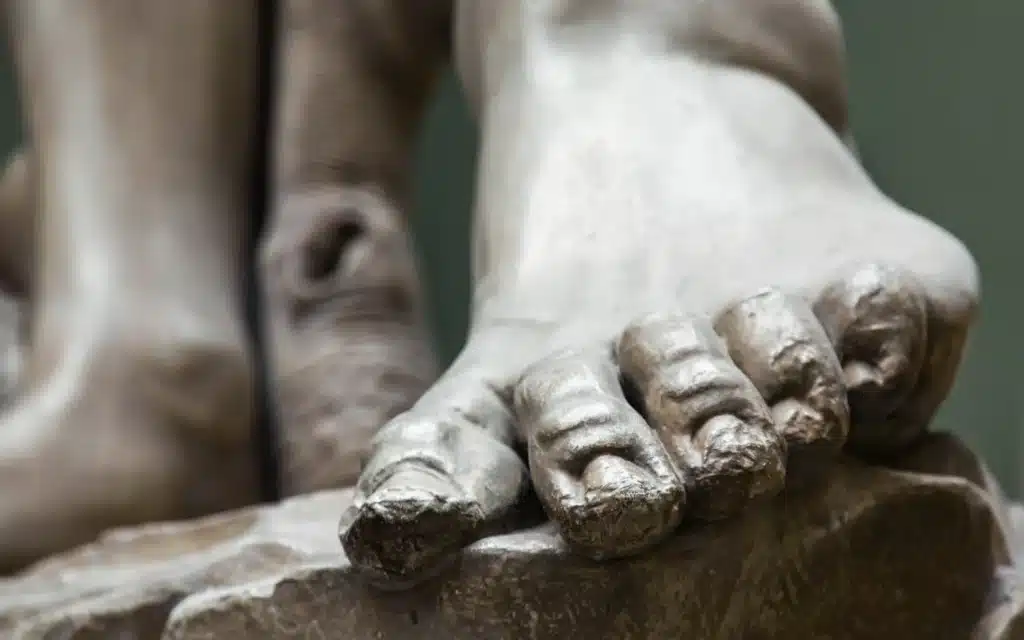 Close-up of a marble statue's foot, its toes resting on the edge of a rough-hewn stone base