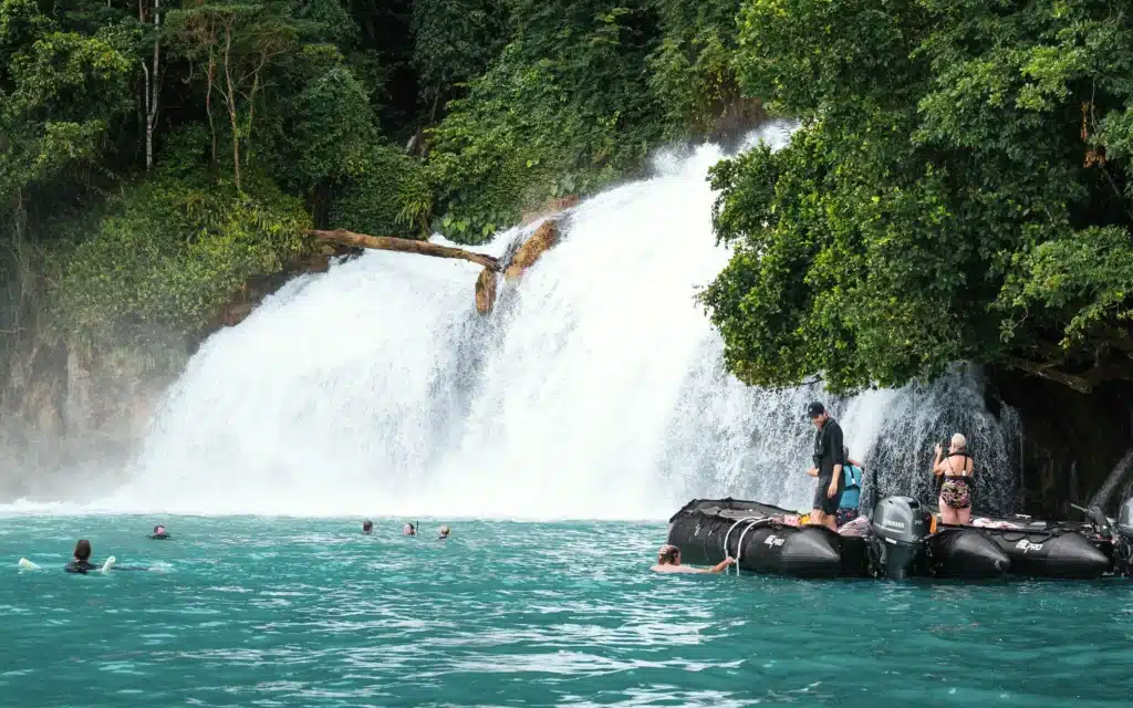 Guests swimming and photographing a jungle waterfall from expedition tenders