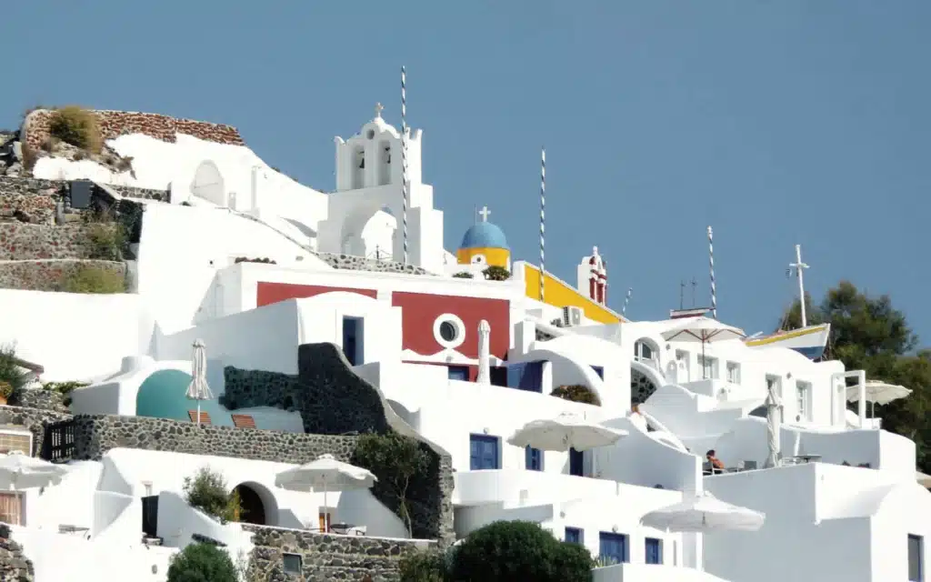 Terraced whitewashed buildings with a white bell tower, a blue dome and red and yellow facades against a deep blue sky