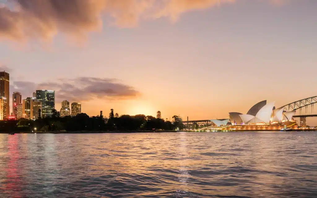 The Sydney Opera House glows at dusk beside the Harbour Bridge