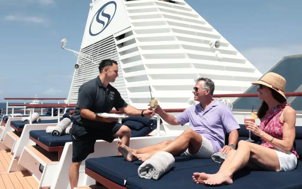 A SeaDream crew member serves cocktails to sunbathing guests on deck