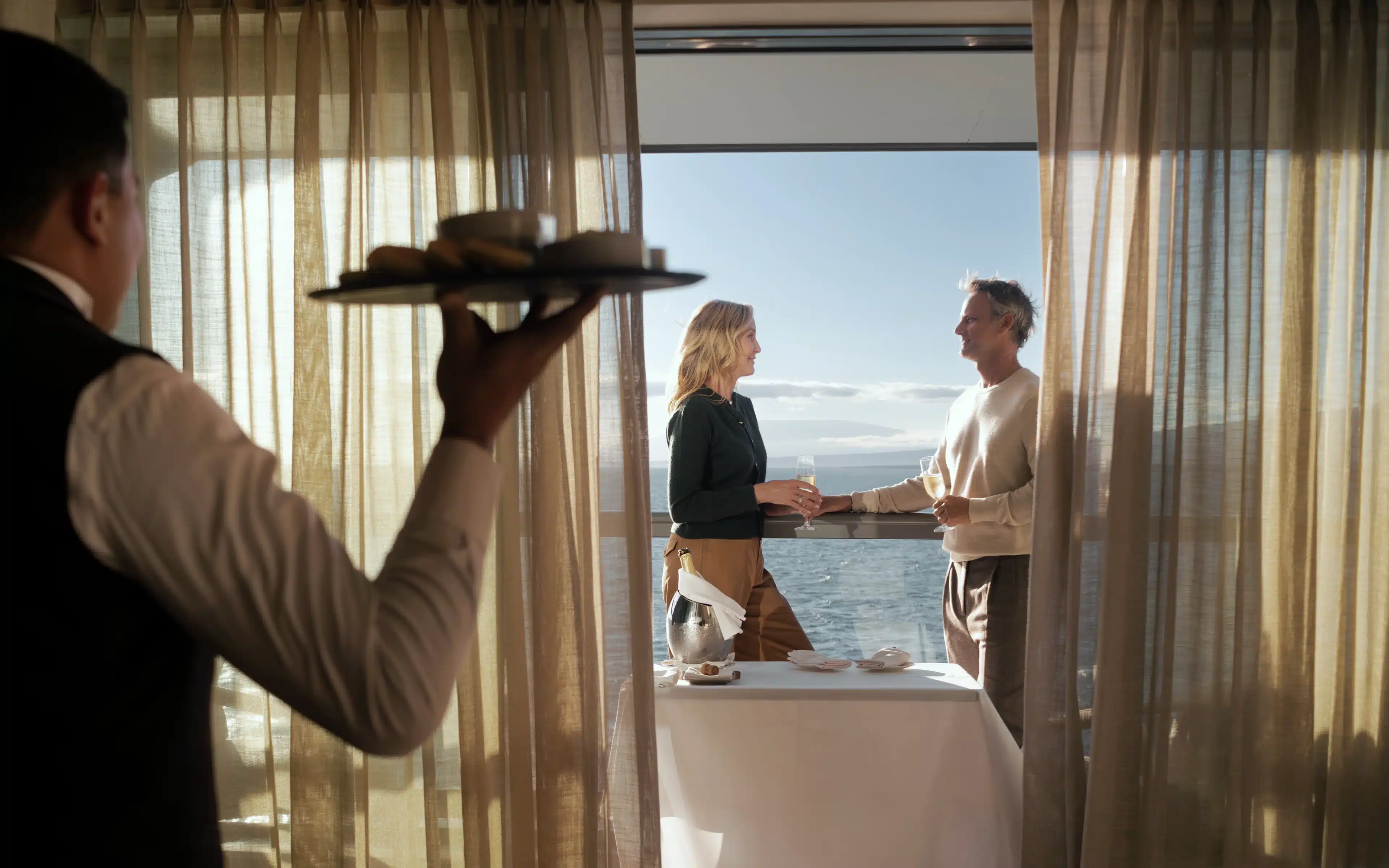 Butler serving canapés to a couple on a Silversea suite balcony at sunset