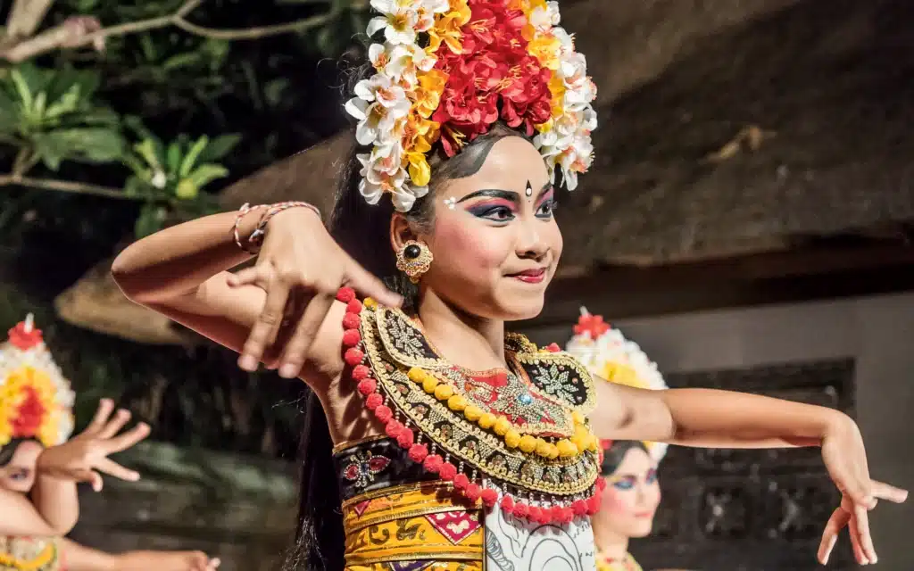 Balinese dancer in a floral headdress and gilded costume performing a traditional dance at night