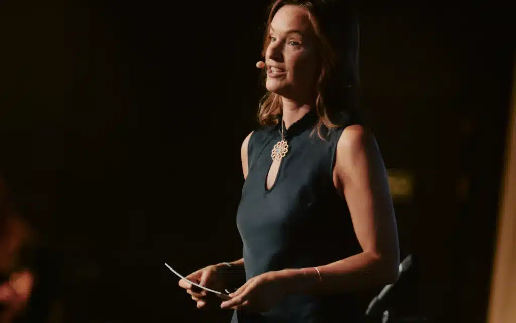 Explora Journeys President Anna Nash speaking on stage with a headset microphone and cue card