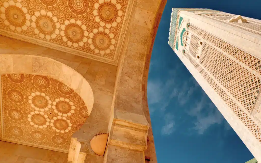Looking up at carved geometric archways and a tall ornate minaret against a blue sky in Casablanca