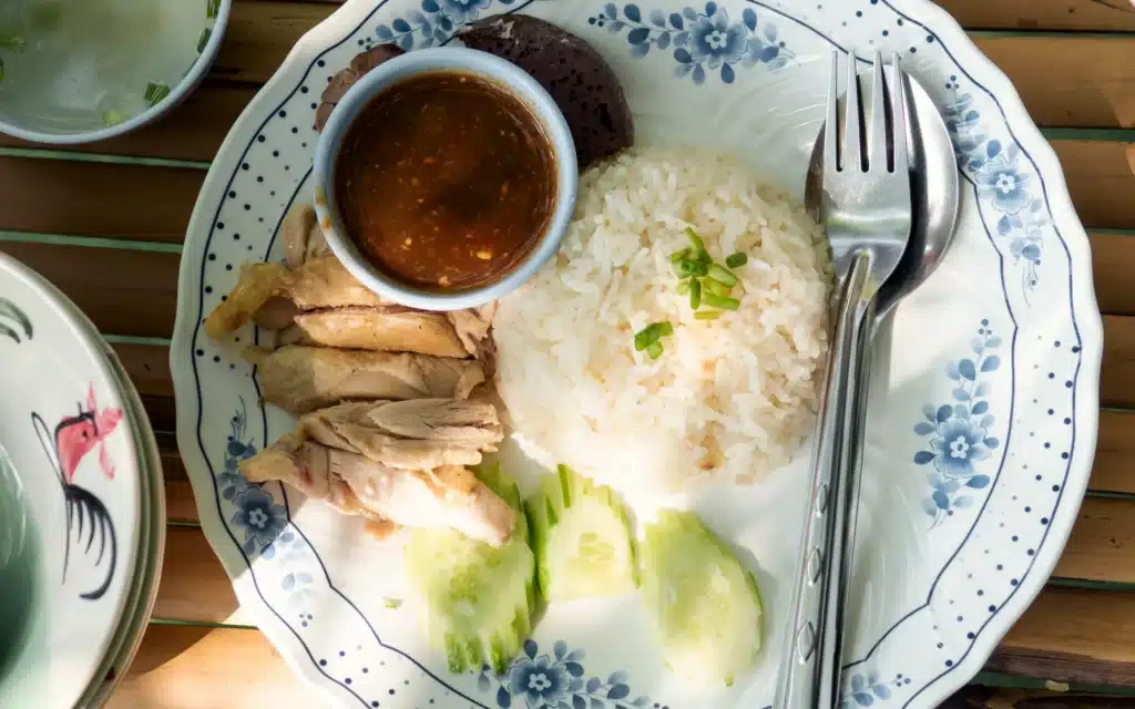 Overhead view of sliced poached chicken, rice, cucumber and dipping sauce on a blue floral plate