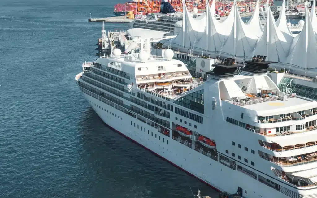 Seabourn Odyssey berthed alongside the white sails of the Canada Place cruise terminal in Vancouver, with container cranes in the distance